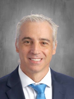 Dr. Ursone is wearing a white shirt and a blue suit blazer.